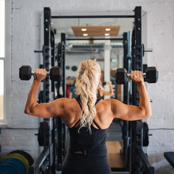 A woman working out with a personal trainer lifting dumbbells